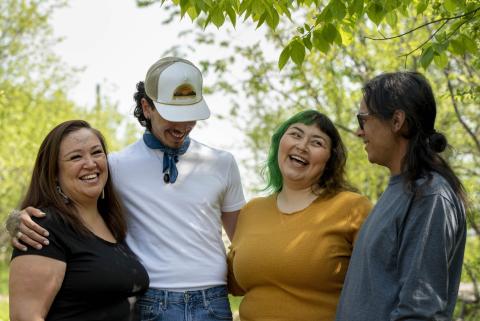 A group of four Indigenous youth smiling and laughing in nature. 